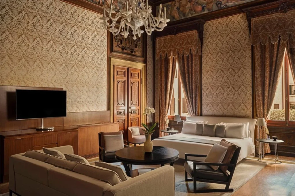 Elegant suite with ornate Venetian decor, patterned wallpaper, wood paneling, classic furnishings, and a comfortable bedroom and living area at Aman Venice