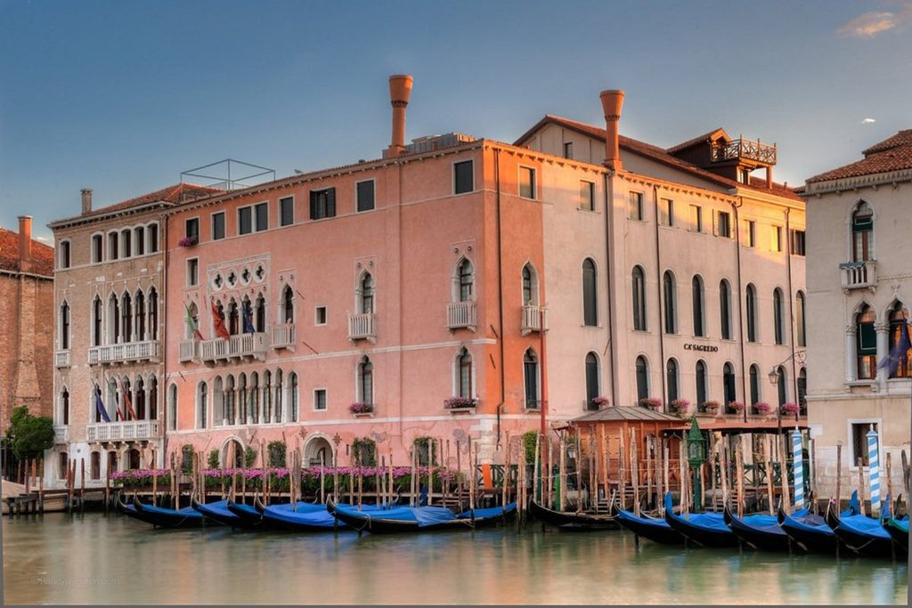 Elegant historic palace glowing in the evening light with traditional gondolas moored along the waterfront – Ca’ Sagredo Hotel, Venice.