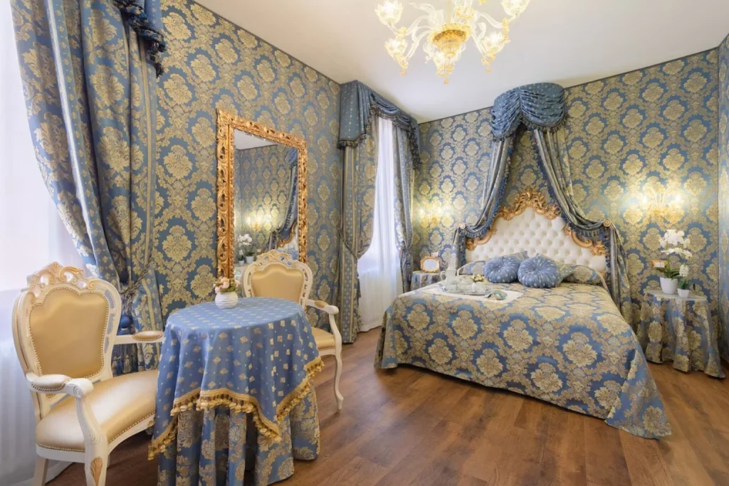 Elegant Venetian-style bedroom featuring blue-and-gold damask décor, ornate furniture and a lavish canopy bed – Canal View San Marco Luxury Rooms, Venice.