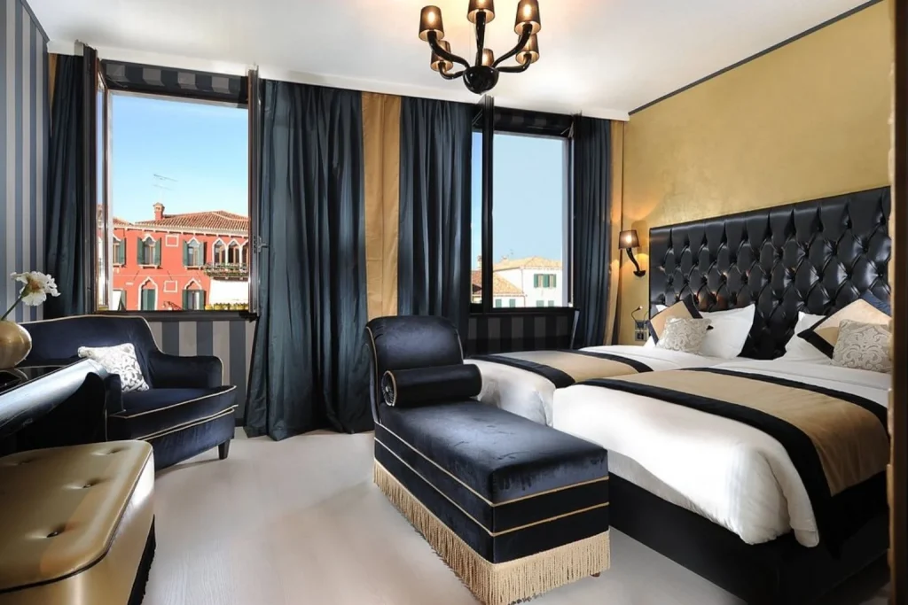 Elegant guest room with twin beds, sophisticated black and gold décor and views of traditional Venetian architecture, Carnival Palace Hotel, Venice.