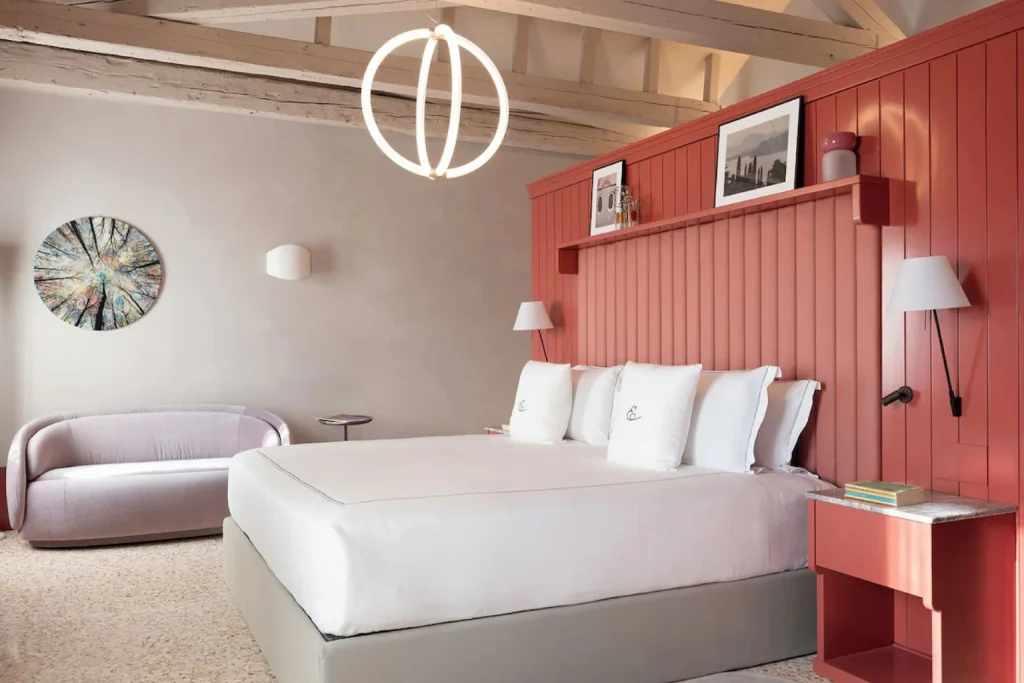 Elegant bedroom with exposed ceiling beams, contemporary furnishings and a distinctive red panelled wall at Elizabeth Unique Venice in Venice.