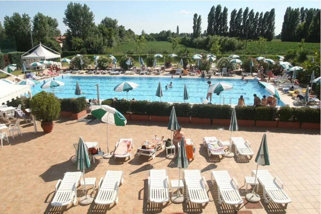 Large outdoor swimming pool at Green Garden Resort with sun loungers, umbrellas and surrounding greenery near Venice.