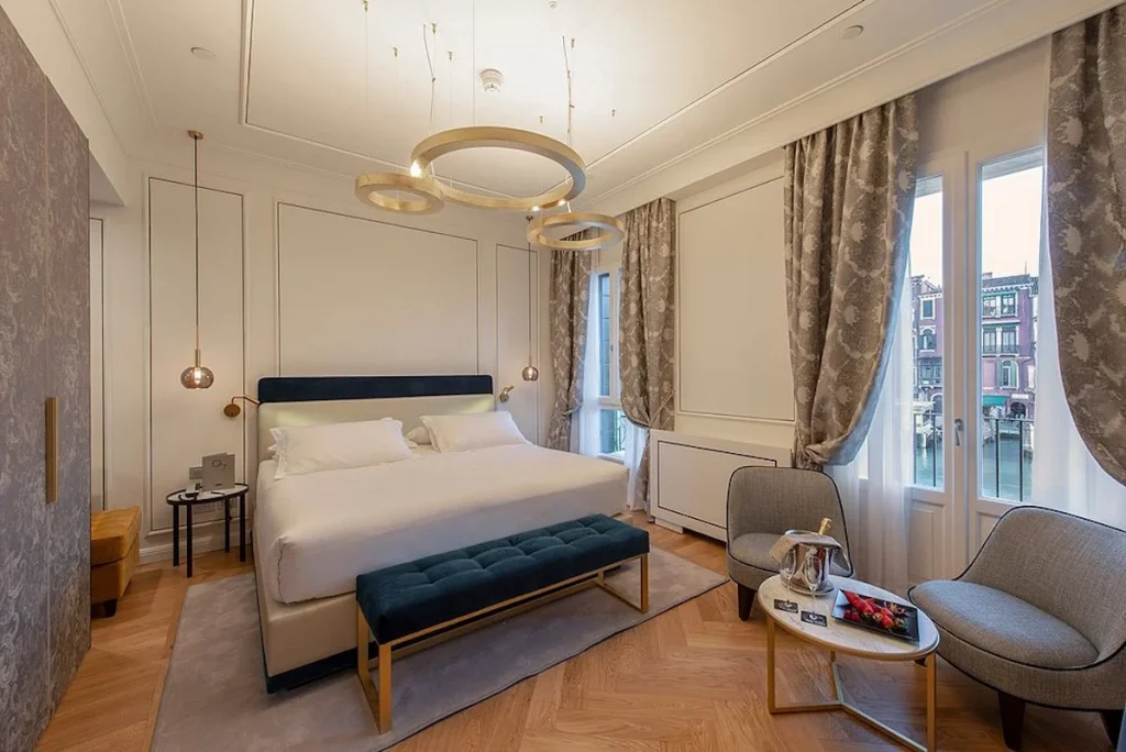 Modern canal view room with contemporary décor, elegant furnishings, and large windows overlooking a Venice canal at H10 Palazzo Canova in Venice, Italy.