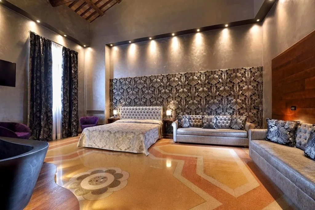 Spacious guest room with high ceilings, elegant patterned décor, a double bed and comfortable seating area, Hotel Abbazia, Venice.