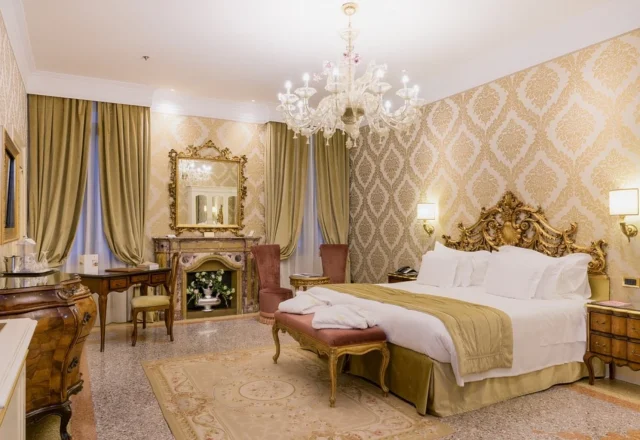Luxurious Venetian bedroom with an ornate carved bed, crystal chandelier, damask wallpaper and antique-style furnishings – Hotel Ai Reali – Small Luxury Hotels of the World, Venice