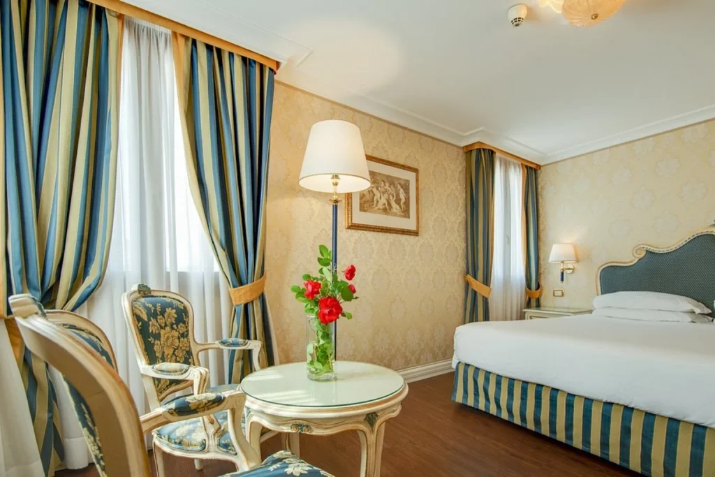 Bright guest room with traditional Venetian furnishings, striped fabrics and elegant seating at Hotel Antiche Figure in Venice.