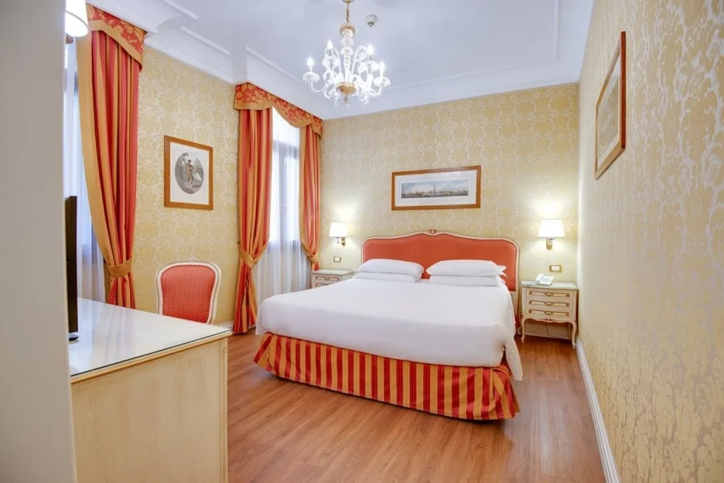 Elegant hotel room with red and gold Venetian décor, chandelier and large double bed, Hotel Antiche Figure, Venice