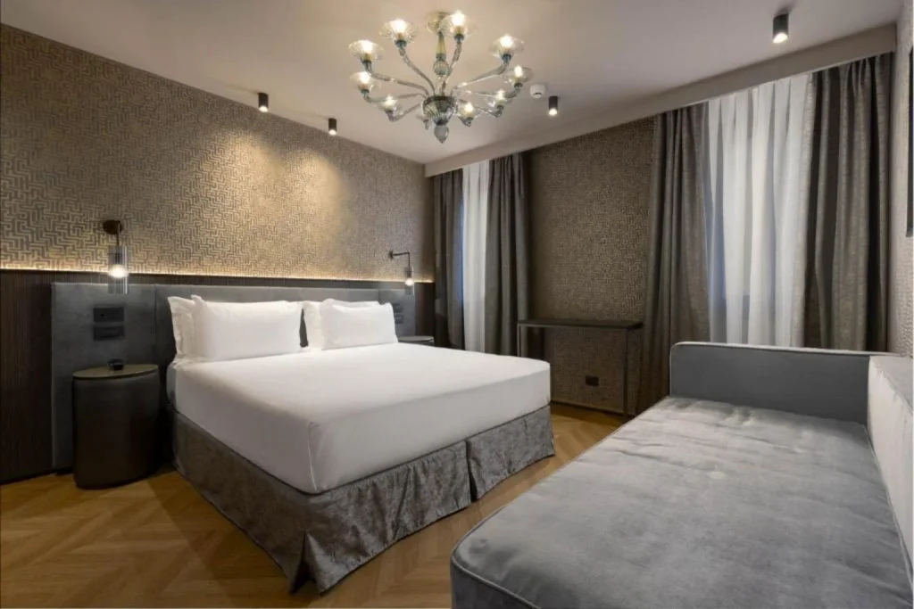 Modern hotel room with large double bed, grey décor, sofa and decorative chandelier, Hotel Atmosphere, Venice