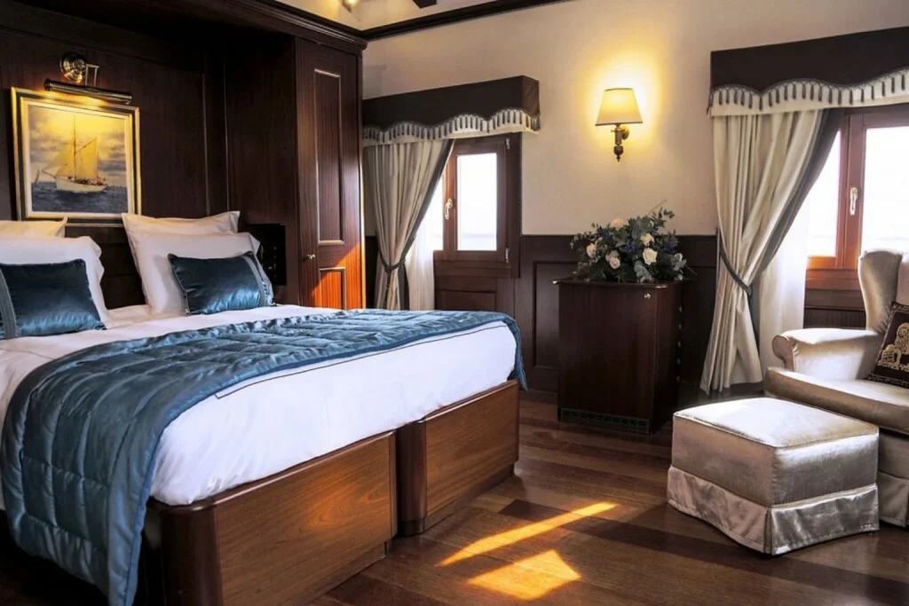 Elegant guest room with rich dark wood furnishings, blue accents and comfortable seating by the windows, Hotel Bucintoro, Venice.