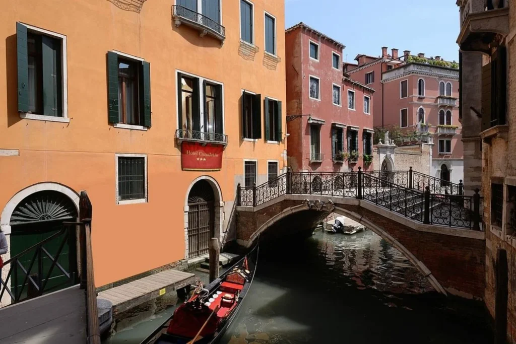Picturesque Venetian canal with a gondola, elegant footbridge and colorful historic buildings beside the hotel – Hotel Canaletto, Venice.