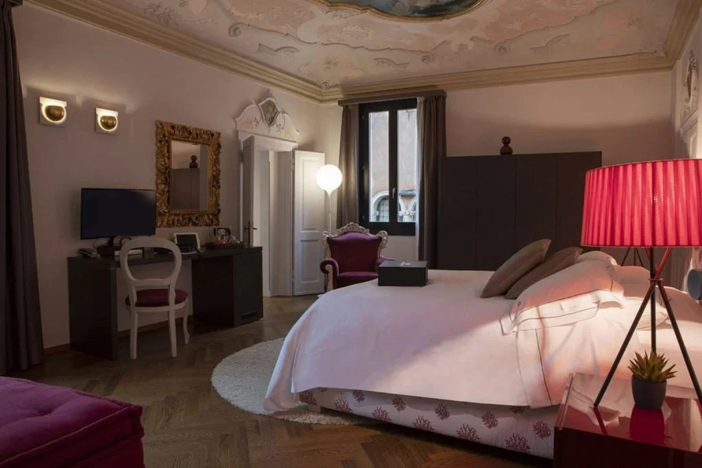 Elegant guest room blending contemporary furnishings with historic ceiling details and distinctive pink accents, Hotel Corte di Gabriela, Venice.