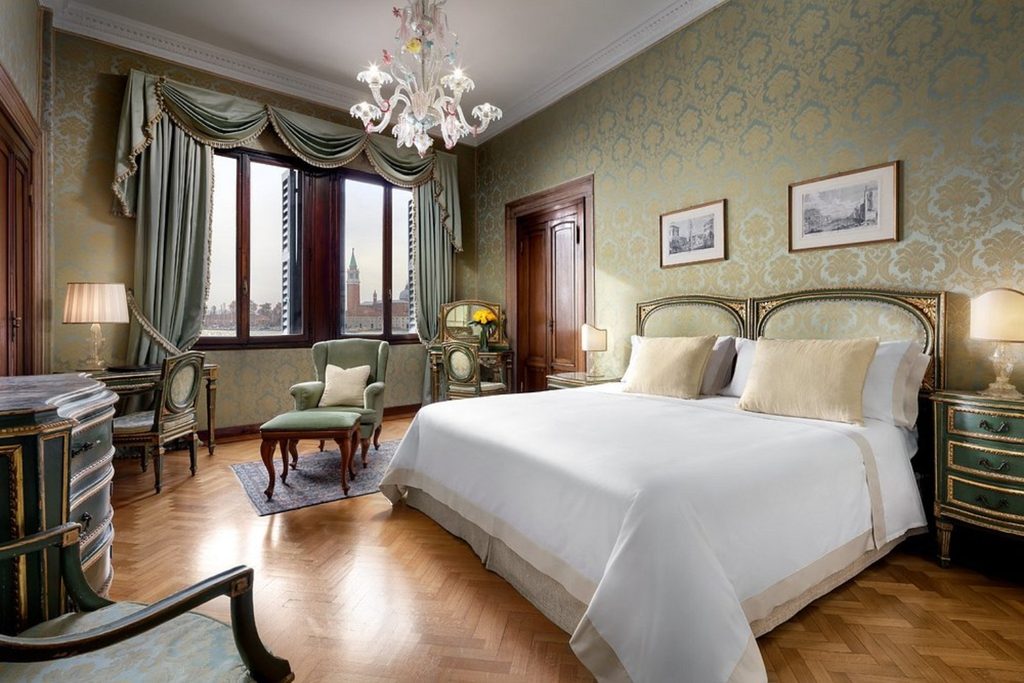Elegant bedroom with classic Venetian furnishings, Murano-style chandelier and views across Venice at Hotel Danieli, a Four Seasons Hotel.
