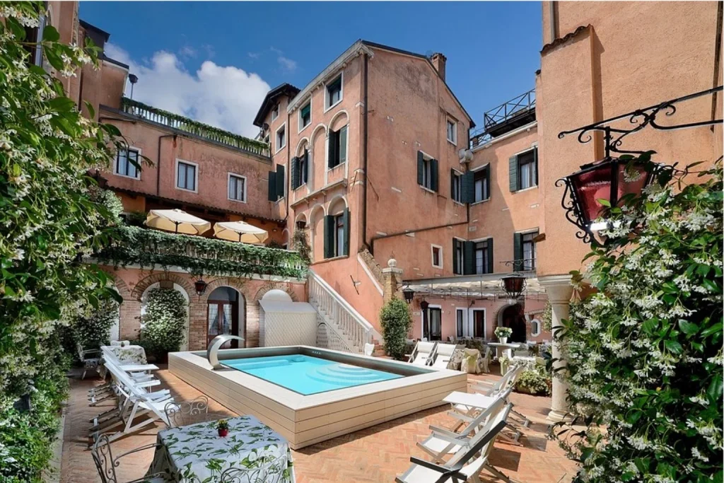 Intimate courtyard pool surrounded by historic Venetian architecture, greenery and sun loungers at Hotel Giorgione in Venice.