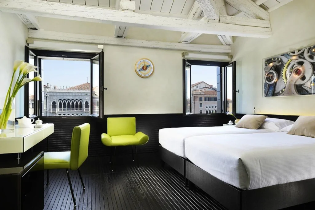 Bright modern bedroom with exposed ceiling beams, contemporary furnishings and views over historic Venice at Hotel L’Orologio Venezia.