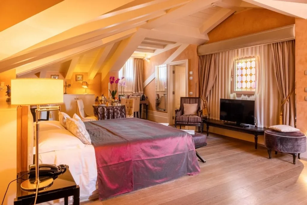 Elegant attic hotel room with exposed ceiling beams, large bed and warm Venetian décor, Hotel Moresco, Venice