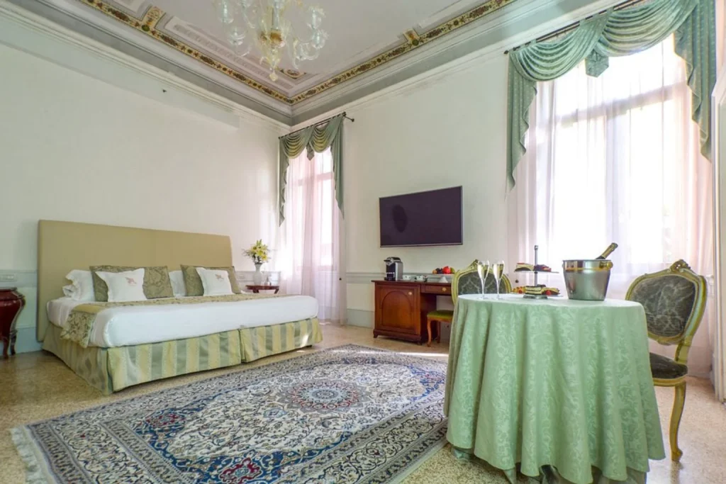 Elegant hotel room with a large bed, ornate ceiling details, classic furnishings, and a dining table at Hotel Palazzo Vitturi in Venice