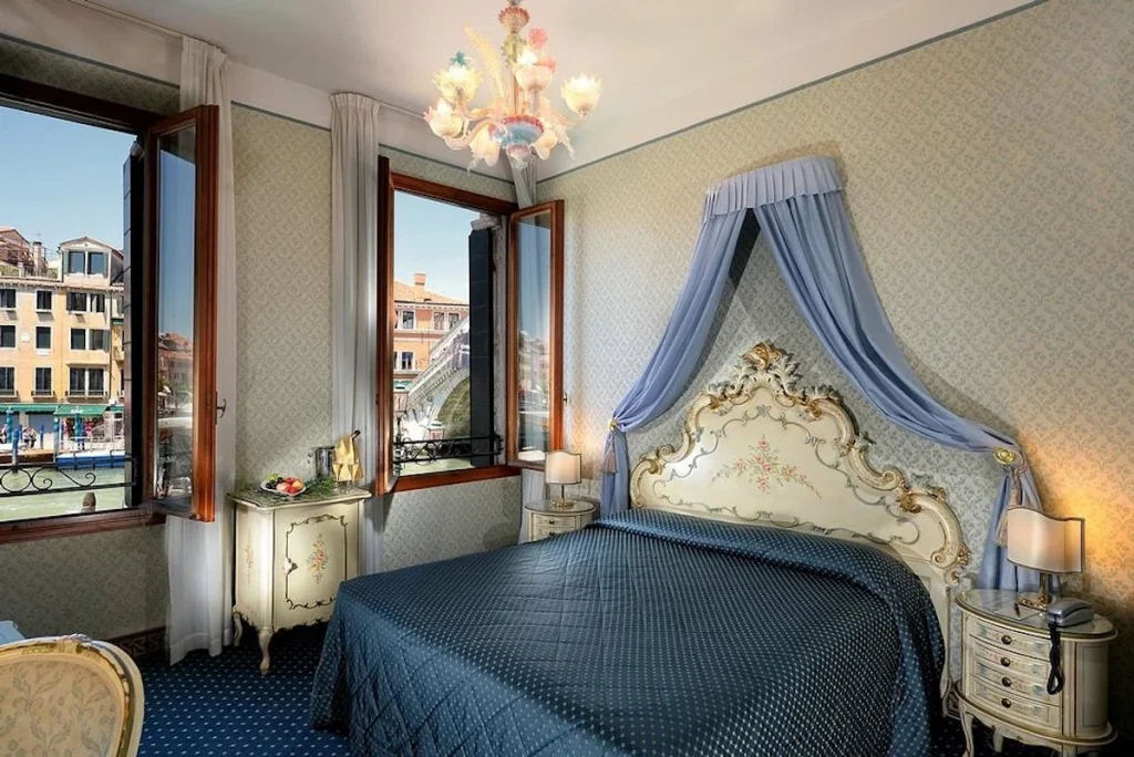 Classic canal view room with Venetian décor, an ornate canopy bed, and views of the Grand Canal at Hotel Rialto in Venice, Italy.