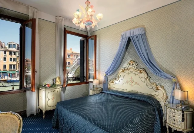 Classic canal view room with Venetian décor, an ornate canopy bed, and views of the Grand Canal at Hotel Rialto in Venice, Italy.