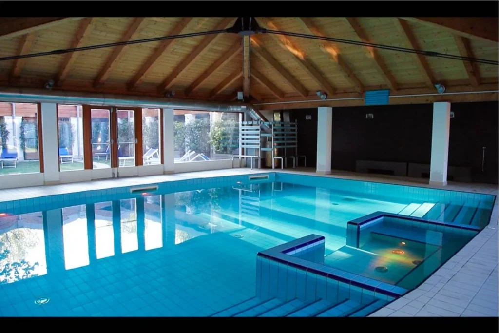 Spacious indoor swimming pool with integrated spa area, large windows and a warm timber ceiling at Camping Venezia in Venice.