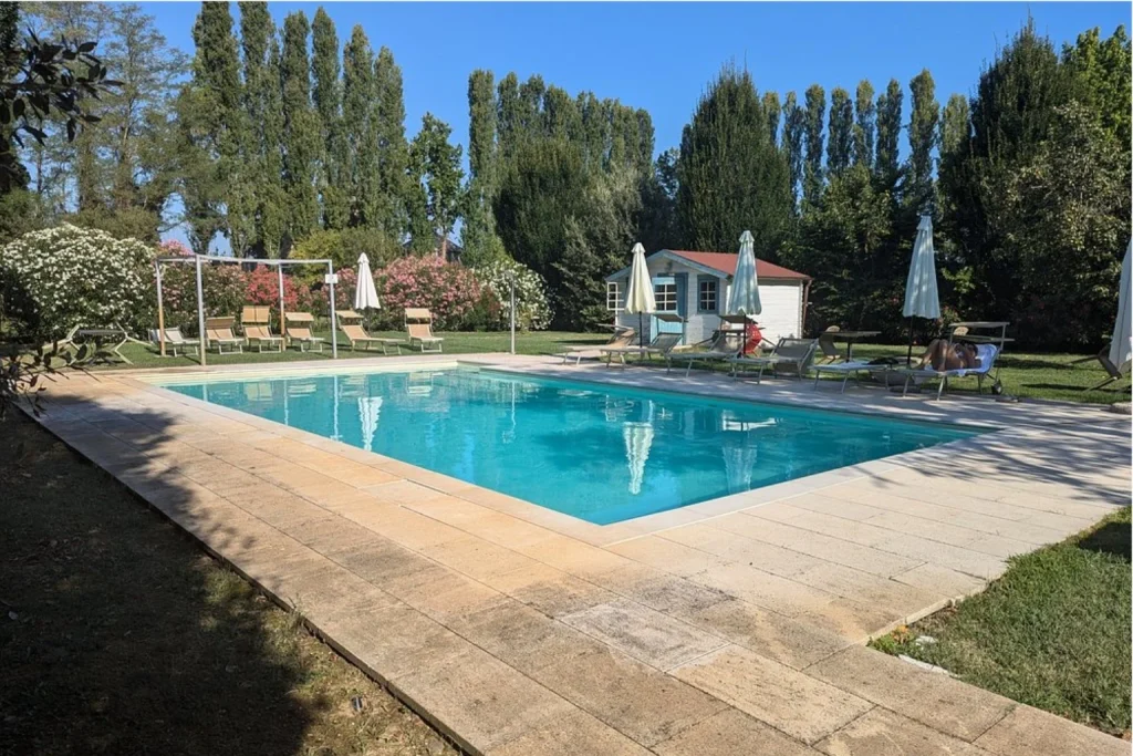 Peaceful outdoor swimming pool surrounded by mature trees, gardens and sun loungers at Ca’ Tessera in Venice.