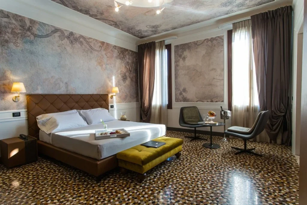 Spacious boutique hotel bedroom with a king-size bed, decorative wall murals, seating area and traditional terrazzo floor – Riva Del Vin Boutique Hotel, Venice