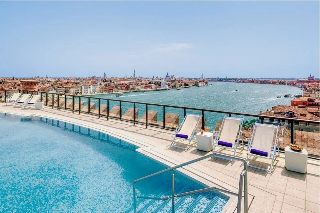 Rooftop swimming pool with sun loungers and sweeping views across the Venetian Lagoon and historic skyline at Hilton Venice in Venice.