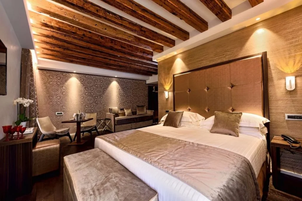 Elegant guest room with exposed wooden ceiling beams, a large bed and warm contemporary Venetian-inspired décor, Rosa Salva Hotel, Venice.