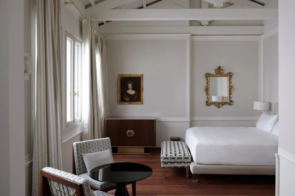 Elegant bedroom at Violino D’Oro Venezia featuring refined neutral interiors, exposed ceiling beams, classic artwork and contemporary furnishings.